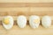 Four cooked and peeled chicken eggs lie on a cutting board on a wooden background. You can see the yolks. The protein is