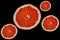 Four cut bright red orange halves grapefruit slices, circles of different sizes on black backdrop