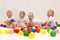 Four cute funny babies sitting on the white blanket and playing colorful balls. Infant party.