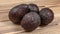 Four dark brown ripe avocados on wooden boards table
