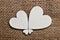 Four diferent size white wooden hearts assembled to flover shape on roug canvas textil background