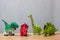 Four dinosaurs toys standing on a wooden floor.