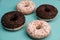 Four donuts, chocolate and white on a turquoise background