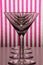 Four empty glasses for martini and vermouth standing in line with white and pink striped background.