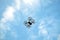 Four engine drone with engine protection grid flying far in the blue sky with calm white clouds