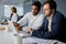 Four focused young multiracial business people in businesswear working on laptops at desk in office