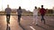 Four friends are running by empty parking zone outdoors - fun happiness, young men and women are running in the evening