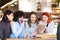 Four friends sitting at a cafe bar looking at tablet. Positive and smiling face expressions