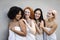 Four girls of different races, dressed in beige towels, stand against a grey wall