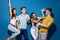 Four good-looking friends are laughing while standing in front of the blue wall having confident and happy looks