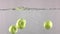 Four green apples fall down in water against gray background, super slow motion