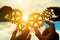 Four hands of businessmen assemble gears into a puzzle in a single whole against the backdrop of the sunset, business concept idea