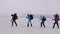 Four hikers are walking on each other over snow field in cold winter day, helping to themselves by sticks