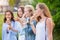 Four joyful young girlfriends standing in a row smiling happily eating ice cream in Park