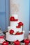 Four-layer white wedding cake with red roses and strawberries