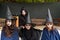 Four little girls in carnival costumes of witches and zombies look at the camera and smile against the backdrop of an abandoned