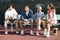Four mixed doubles tennis players sitting at tennis court front view