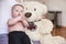 Four months old baby boy sitting on her mother knees, large plush teddy bear next to him