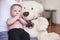 Four months old baby boy sitting on her mother knees, large plush teddy bear next to him