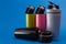 Four multi-colored thermal bottles of shaker for sports nutrition on a blue background