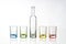 Four multicolored empty shot glasses and small bottle placed symmetrically on a white background.