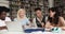 Four multiracial schoolmates communicating sit in library with laptop