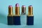 Four old used tubes of lipstick stand on a blue background.