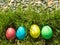 Four painted and decorative Easter eggs in the grass. Top view, copy space