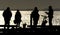 Four people in silhouette talking on seaside pier.