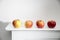 Four red apples are stands on a white mantel