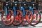 Four rental bicycles lined up with red rims on sidewalk