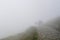 Four silhouettes of people in thick fog on rocky hiking trail in the mountains