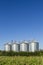 Four silver silos in field under blue sky