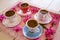 Four small cups of traditional foamy Turkish Coffee serving on a colorful flowery pink tray