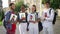 Four smiling confident multiethnic students standing with paperwork outdoors at university campus turning looking at