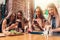 Four smiling female students sitting in cafeteria chatting using mobile phones