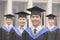 Four smiling university graduates in graduation gowns and mortarboards, looking at camera