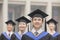 Four smiling university graduates in graduation gowns and mortarboards, looking up