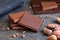 Four squares of dark and milk chocolate with small chocolate bits on grey slate next to cocoa beans. Blurred chocolate in the