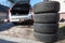 Four summer tyres lying on land next to opened trunk of silver suv car, seasonal tire change