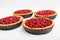 Four tasty homemade cheese tartlets with cherry on white wooden table.