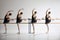 Four teen girls, ballet dancers, training with barre, standing in pose with one leg extended against grey studio