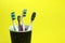 Four toothbrushes in a glass on a yellow background