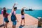 Four tourists waving at an old black pirate boat which is passing by next to a modern marine port