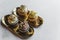 Four various frosted cupcakes with sprinkles arranged on small golden platters on white table. Fancy baked goods. Baking