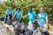 Four volunteers in work overalls collect garbage in forest in plastic bag. Close-up during action. Cleaning of nature from waste.