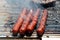 Four well done sausages grilling on the outside charcoal barbeque grill surrounded with smoke and other meat