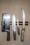 Four well-used chefs knives on a magnetic holder mounted on textured wall