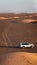 A four wheel drive car and its tyre marking trail are photographed in a desert with sand dunes during morning sunrise