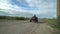 Four wheel drive red and black quad bike standing idle on the grass, with trees and a blue sky with clouds to the rear.